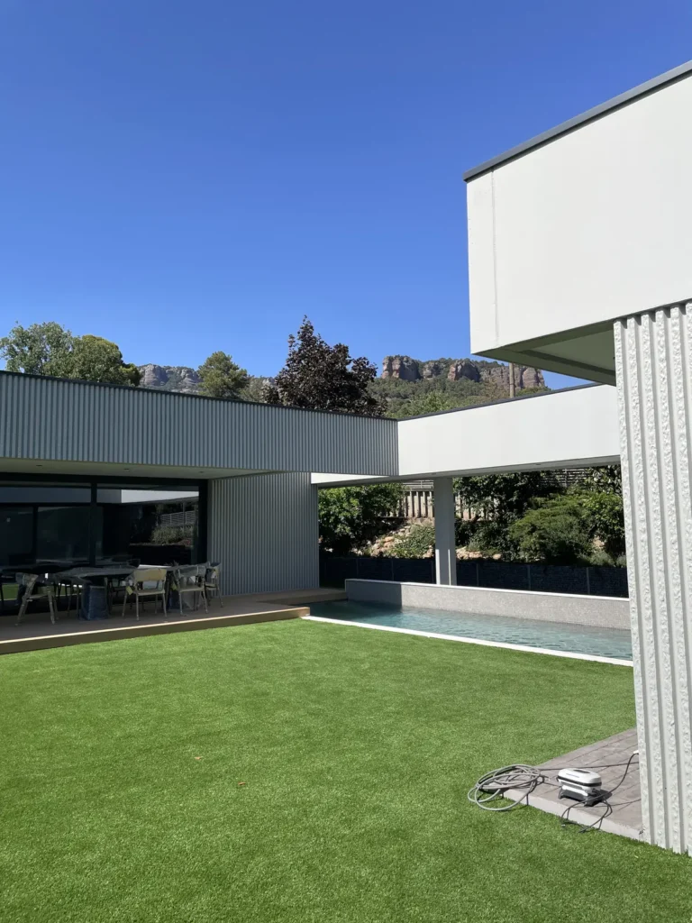 Jardín moderno con césped artificial, piscina y paisajismo realizado por Serveis Jardineria Soler