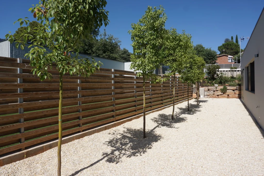 Planificación del espacio en un jardín con árboles, grava decorativa y vallado de madera