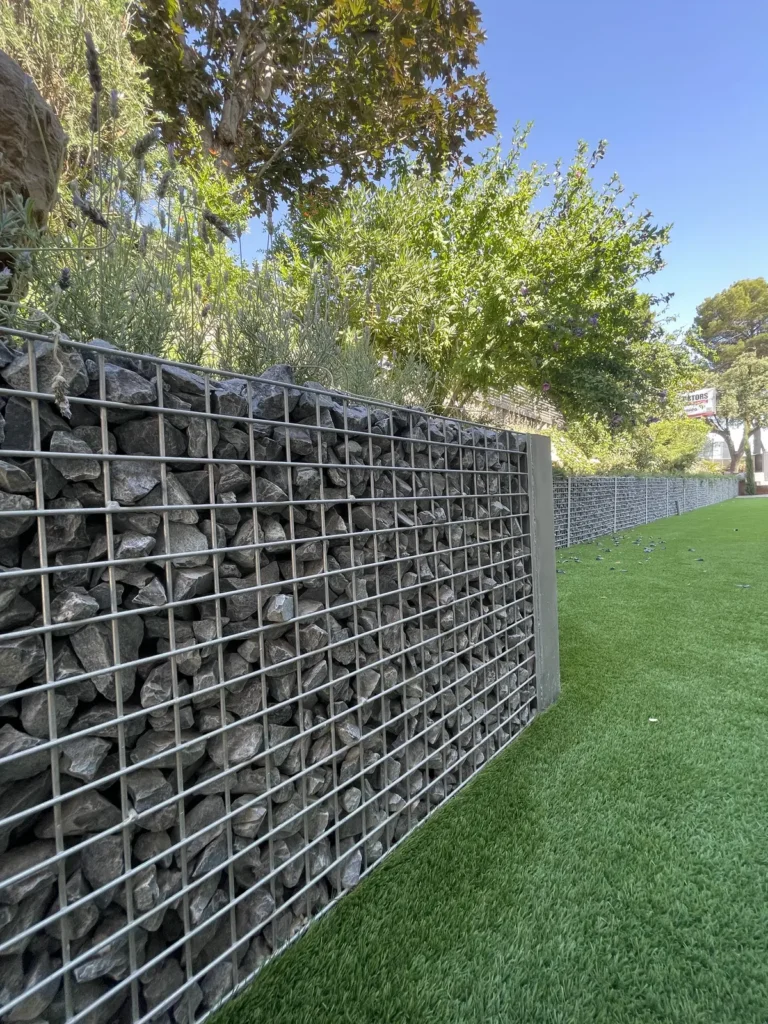 Detalle de los remates del césped artificial junto a un muro de gaviones