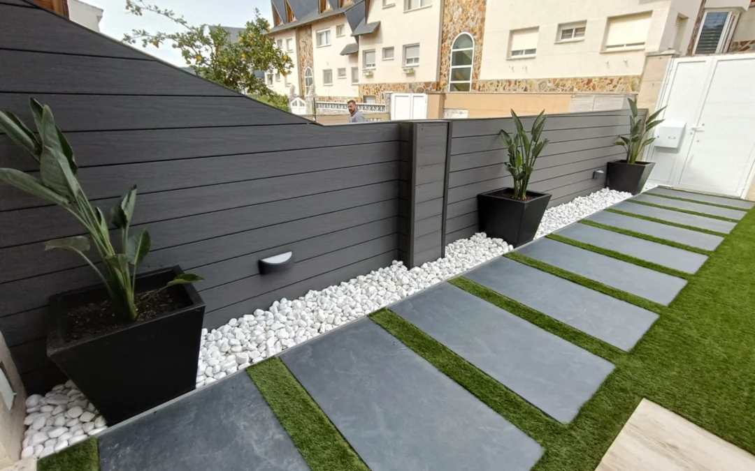 Valla de ocultación de composite gris integrada en un jardín moderno con pavimento y césped artificial